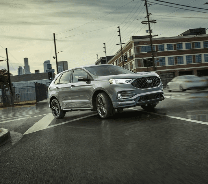 2024 Ford Edge ST SUV in Iconic Silver turning right on a wet street