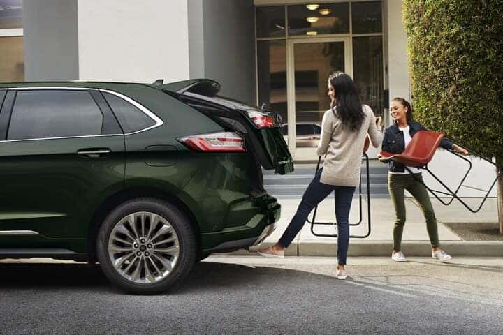 Two women carrying chairs as one of them activates the hands-free liftgate