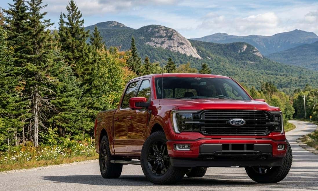 A red 2026 Ford F-150 on a road with a view of forested mountains