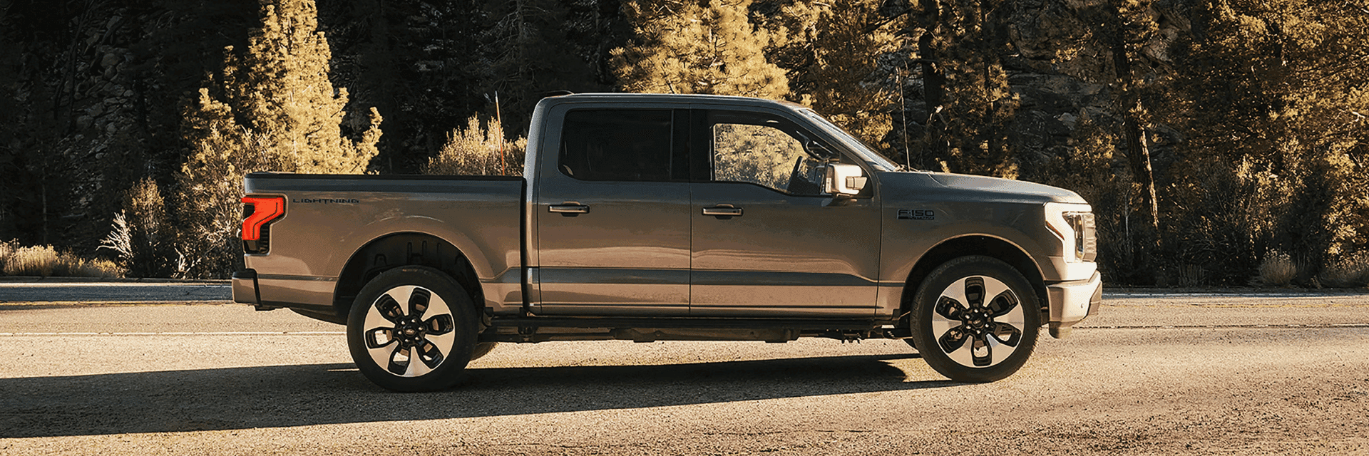 A 2025 Ford F-150® Lightning® in Iconic Silver parked on a paved road showing off the side profile