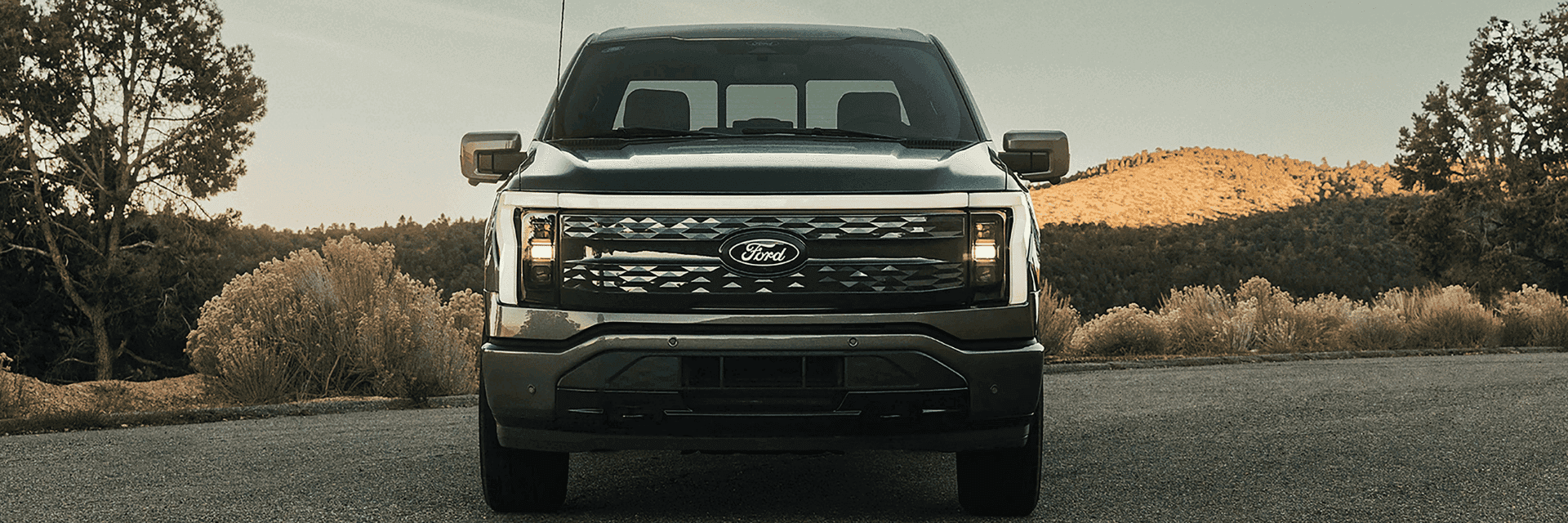 A 2025 Ford F-150® Lightning® in Carbonized Gray parked with a hilly terrain in the background