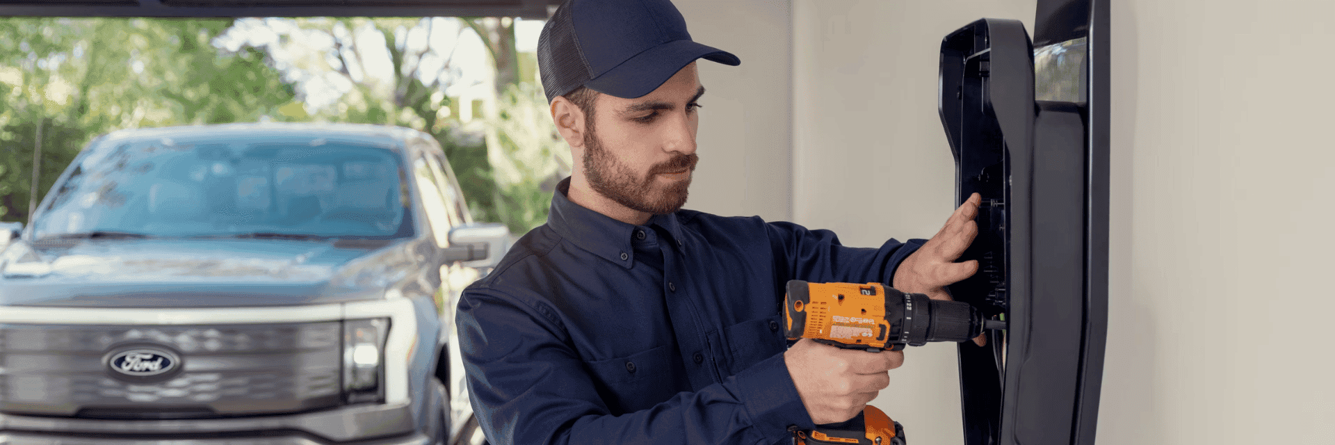 Technician installing a home charger in a garage with a Ford F-150® Lightning® parked in the driveway and visible through the open garage door 