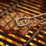seared pork chop in tongs on fiery grill
