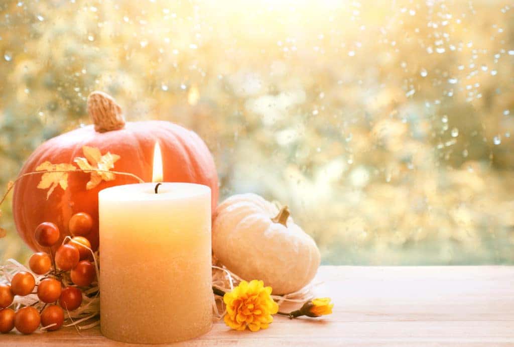 Burning candle with pumpkins by window on a rainy day