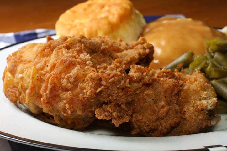 Plate of golden fried chicken with vegetables and a biscuit