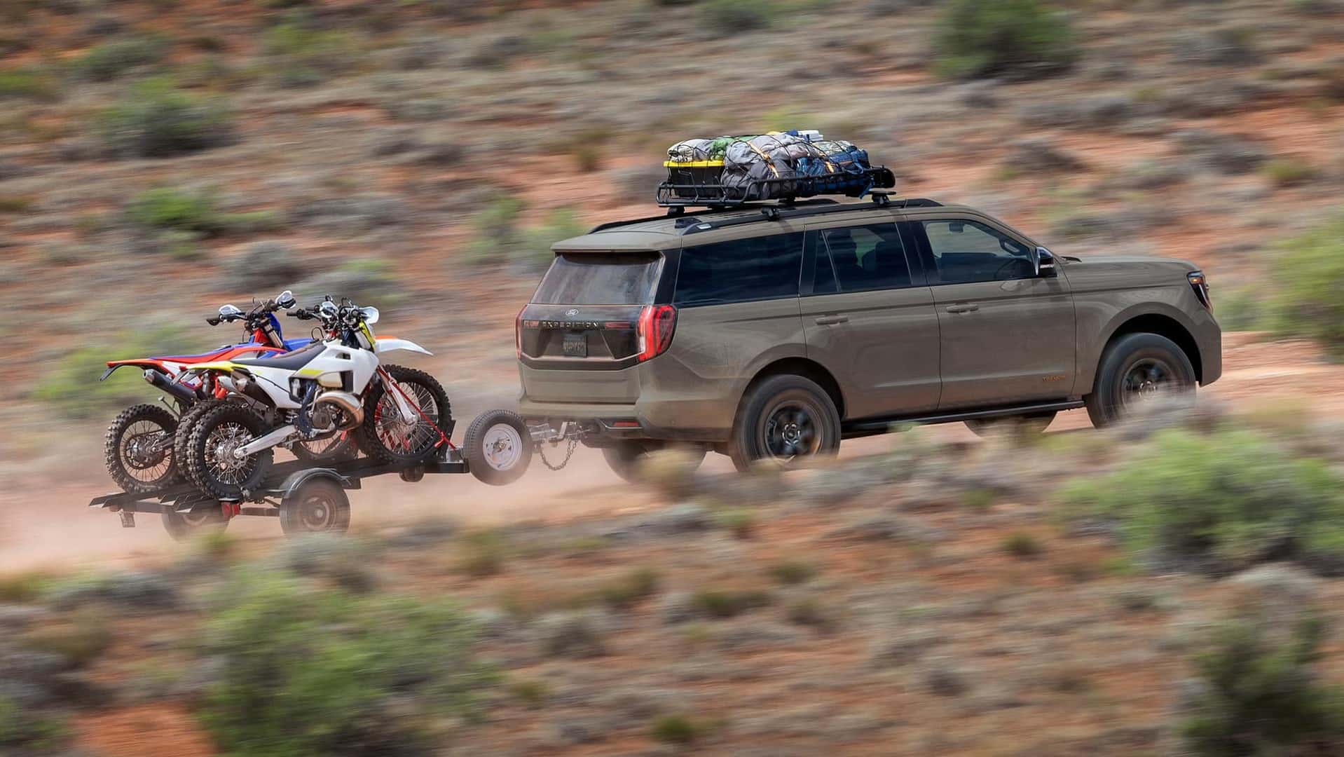 a view of the new 2026 ford expedition towing a small trailer with two dirt bikes loaded on to it.
