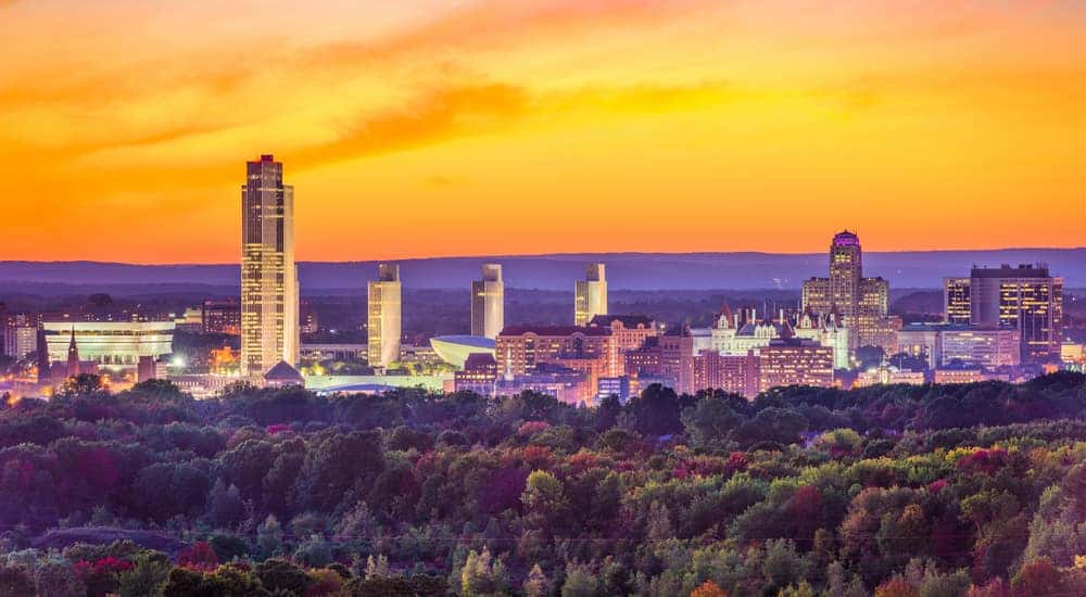 The skyline of Albany, NY, is shown in front of an orange sunset