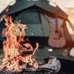 Orange fire in front of a green tent with a guitar leaning against it