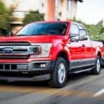 Red Ford F-150 with a trailer hooked on the back driving past houses