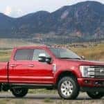 Red 2017 Ford F-250 Super Duty pickup truck parked on a paved road with green fields and dark mountains in the distance