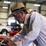 Roush, an older man, working under the hood of a vehicle in a garage