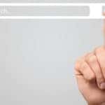 Hand up in front of a grey wall with the pointer finger touching a white "SEARCH" bar floating in the air