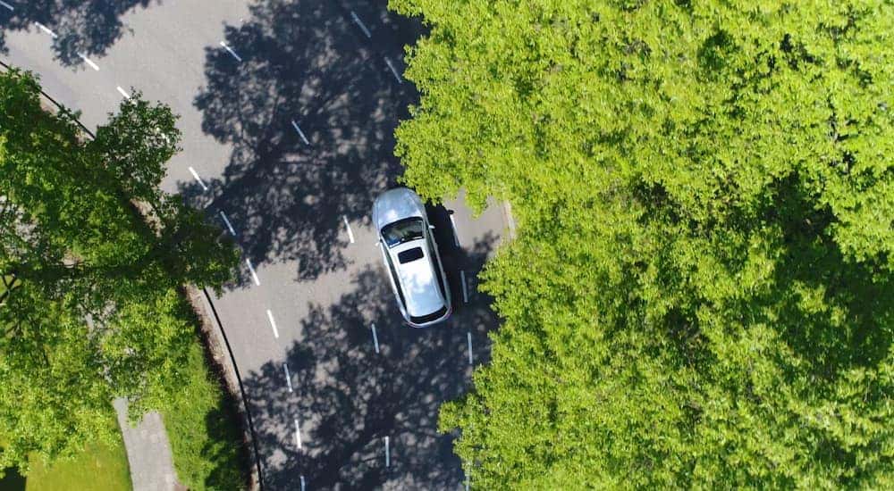 A silver car is shown from a bird's eye view taking a corner on a multi-laned road.