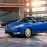 Woman in a purple dress looking at a blue 2018 Ford Focus hatchback parked in a grey and brown showroom