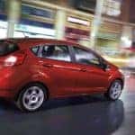 Red 2018 Ford Fiesta hatchback driving down a road next to store fronts