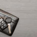 Black wallet with car keys on top of it sitting on a grey wood table