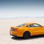 Orange 2018 Ford Mustang parked on flat, light colored ground with mountains in the distance