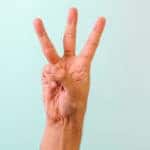 Hand with three fingers up in front of a blue wall