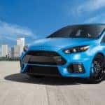 Bright blue 2017 Ford Focus parked on cement with tall buildings in the background