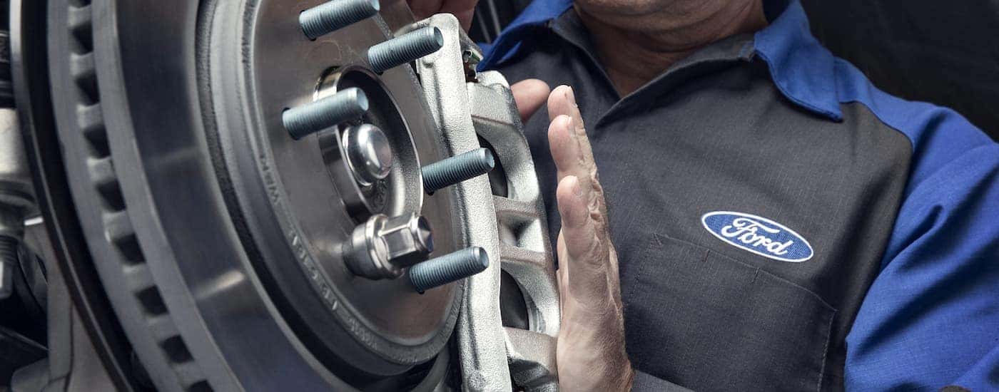 A close up of a mechanic inspecting a rotor is shown at a Ford dealership.