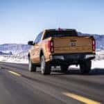 Orange 2019 Ford Ranger pickup truck driving on a paved road toward mountains with snow on both sides of the road