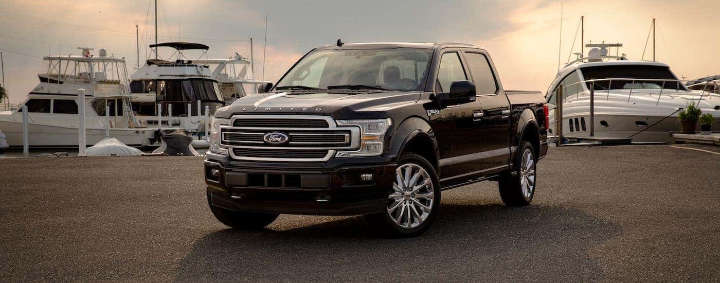 A black 2019 Ford F-150 Limited is parked in front of boats in a marina at sunset.