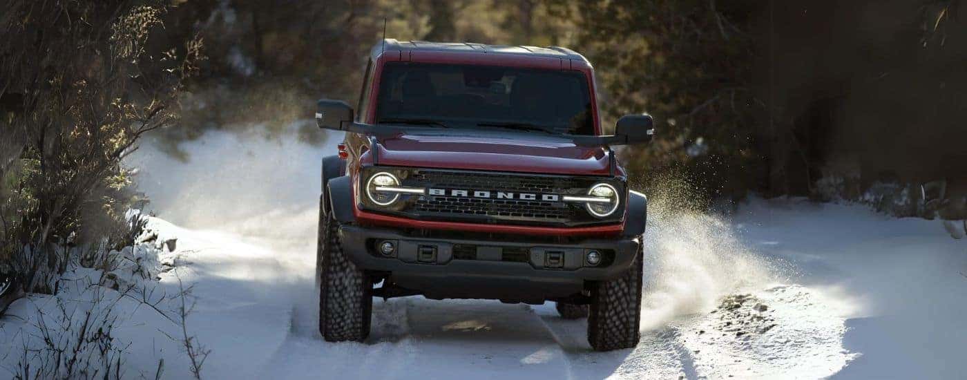 A red 2022 Ford Bronco Wildtrak is shown kicking up snow on a trail.