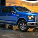 Blue 2016 Ford F-150 parked on a shiny floor in front of a prop screen with a country scene on it