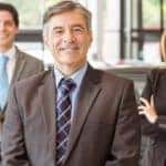 Three smiling sales people are standing in a local car dealers showroom in Albany, NY.