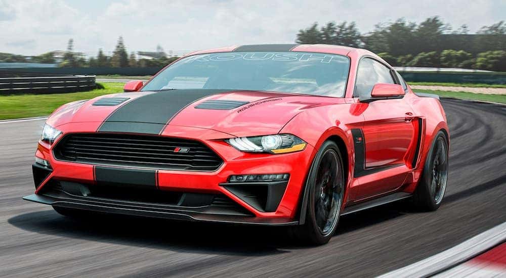 A red and black Ford Mustang is equipped with Roush racing performance parts while racing on a racetrack.