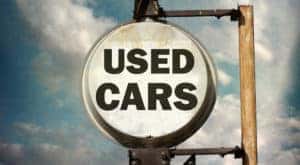 A circular white sign with 'used cars' written on it is shown hanging on a pole.