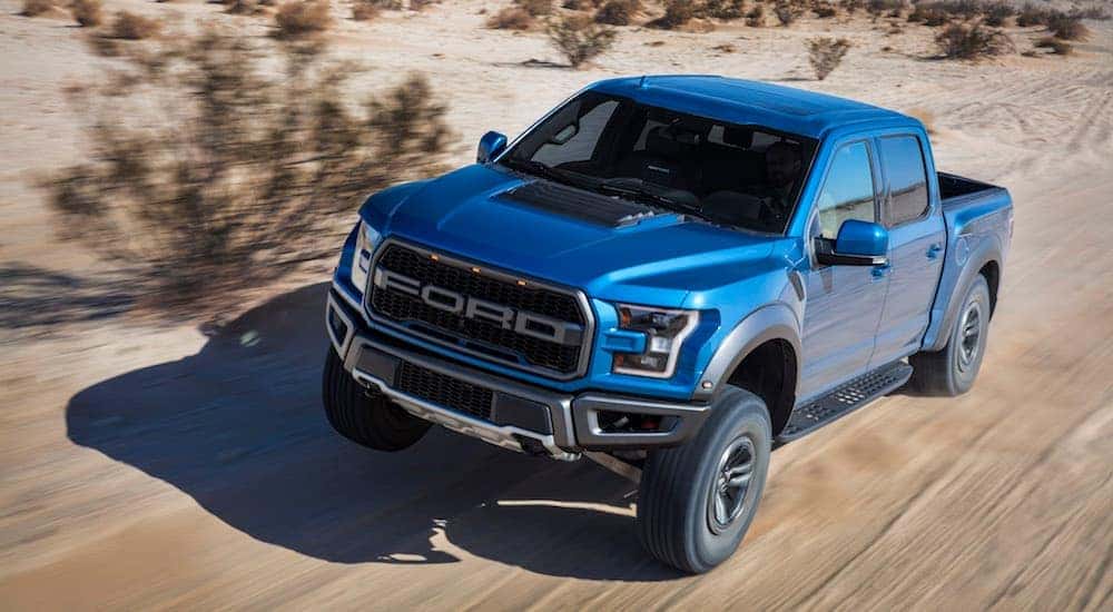 A 2018 Ford F-150 Raptor is shown squatting as it goes up a hill from a high angle.