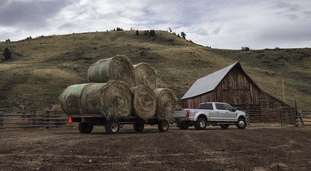 A Silver Ford F-350 truck pulling hay on a trailer in front of a barn after leaving a Ford dealership near you.