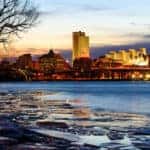 Icy water and a bare winter tree in front of the lit up skyline of Albany NY
