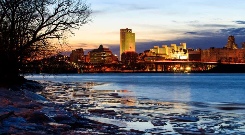Icy water and a bare winter tree in front of the lit up skyline of Albany NY