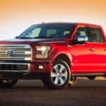 A red 2015 Ford F-150 is parked in an empty parking while the sun sets behind it.