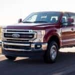 Dark red 2020 Ford F-250 driving on a paved road past a field with mountains in the distance