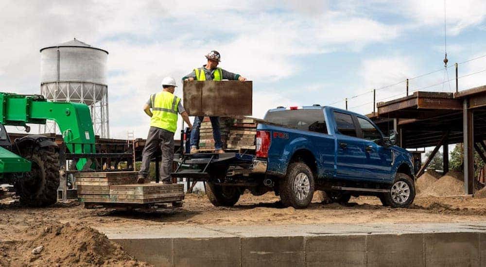 A blue 2020 Ford F-250 Super Duty is shown being loaded with supplies on a construction site.