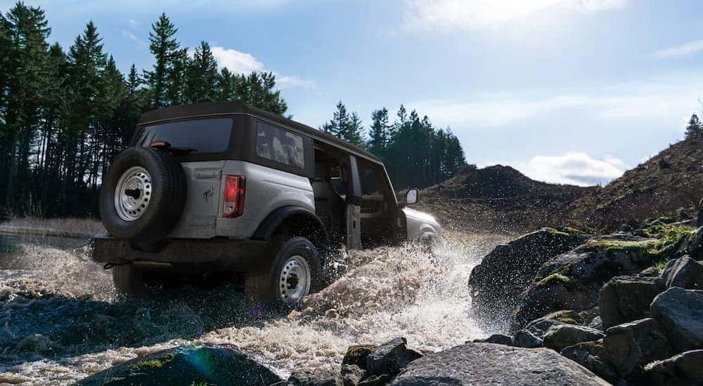 A silver 2021 Ford Bronco is shown from a low angle driving through a creek.