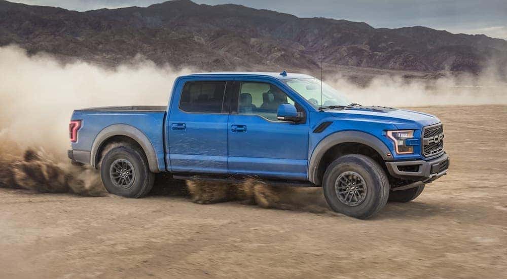 A blue 2020 Ford F-150 Raptor is driving in a desert.
