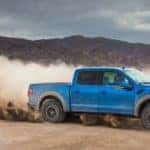 Light blue Ford F-150 pickup truck kicking up dirt in a giant lot with mountains in the distance