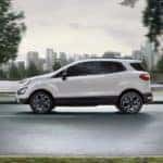 A white 2020 Ford EcoSport is shown from the side driving with a city in the distance.