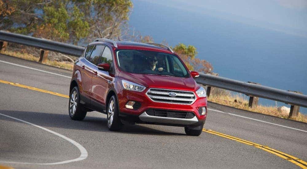 A red 2017 Ford Escape is driving on a winding road on the coast.
