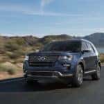Blue used Ford Explorer driving on a paved road next to rocks, water, and mountains