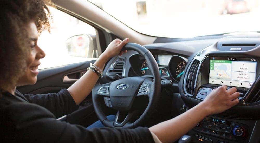 A woman is using the infotainment screen inside her 2017 Ford Escape that is parked in Albany, NY.