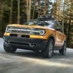 A new Ford SUV hitting the roads, an orange 2021 Ford Bronco Sport, is shown driving on a woodland road.