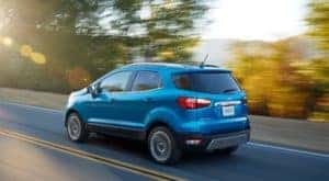 Blue used Ford EcoSport driving on a paved road past trees and mountains after the owner searched ''used Ford Ecosport''.