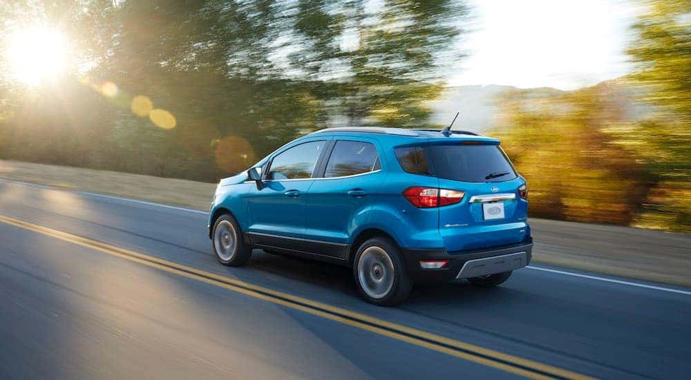 A blue 2018 used Ford EcoSport is driving on a sunny tree-lined road.