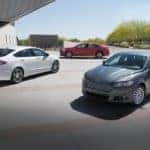 A red, a grey, and a white 2016 used Ford Fusion Hybrid are parked outside of a modern home.