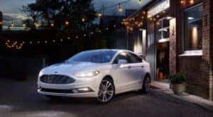 White used Ford Fusion parked under yellow strings of lights and next to a brick building after the owner searched ''used Ford Fusion''.